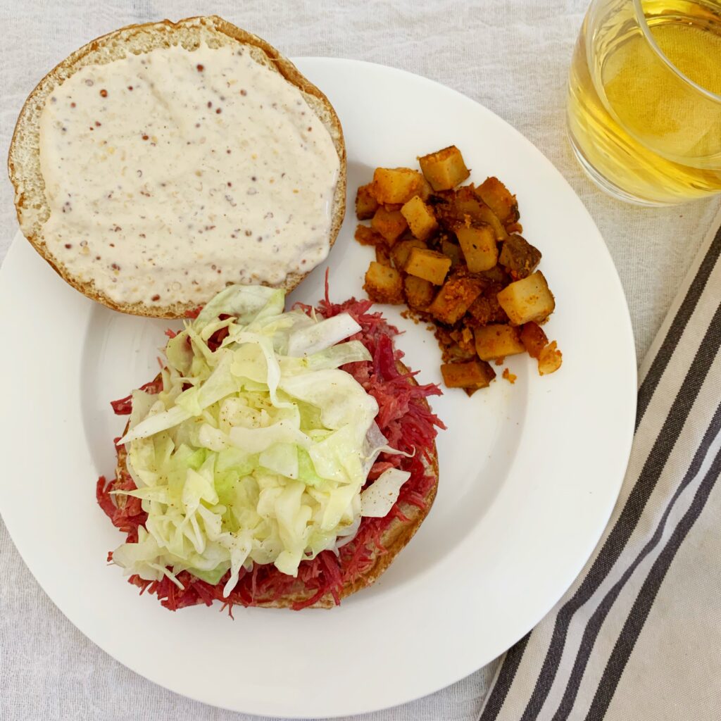 A picture of a corned beef and cabbage sandwich on a plate laying open-faced with potatoes.