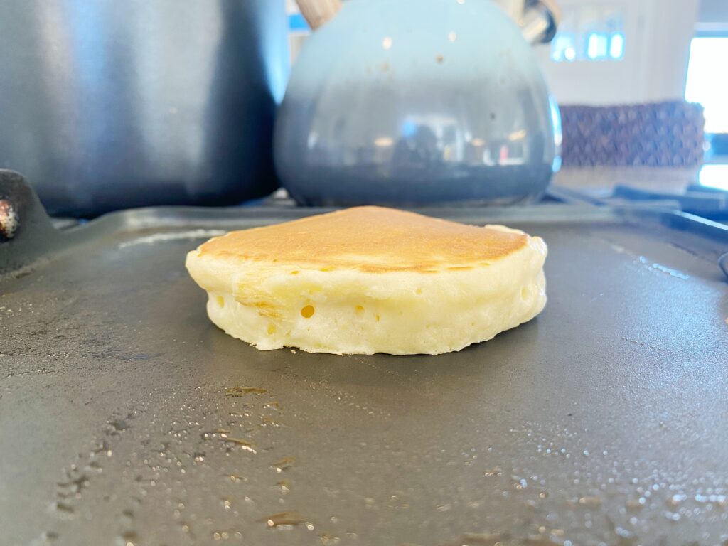 A puffy pancake on the griddle from the side 