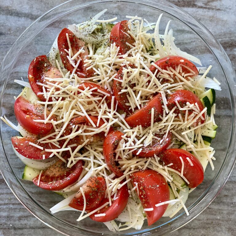 A picture of zucchini, onions, and tomatoes, seasoned and topped with parmesan cheese