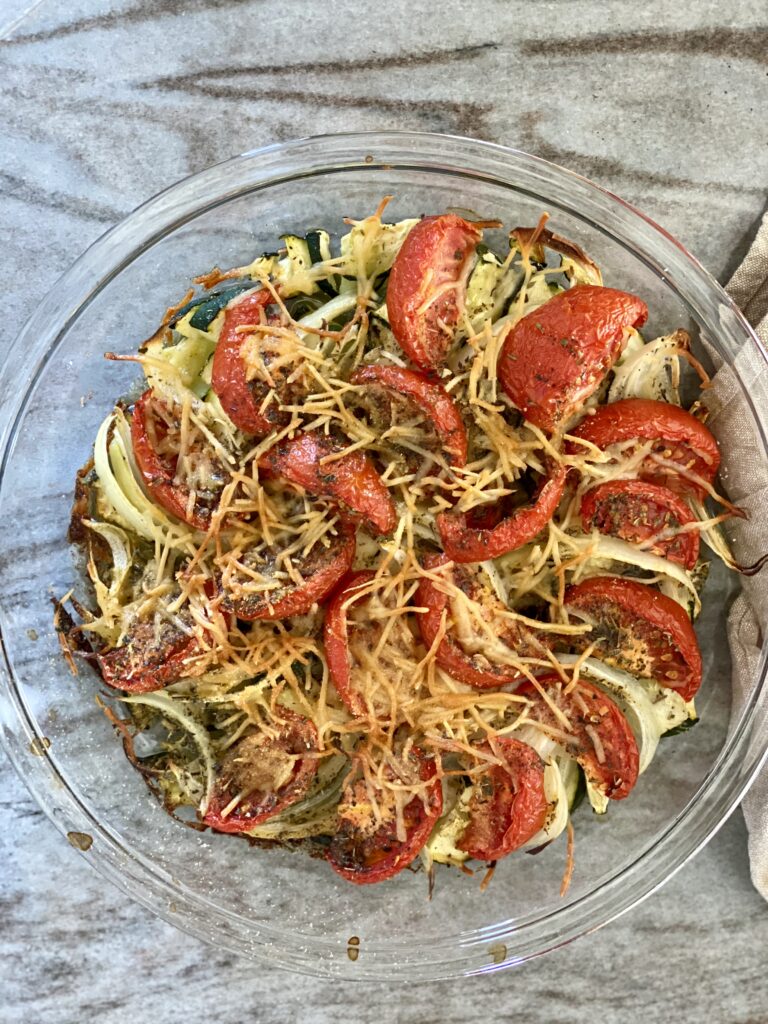 A picture of roasted zucchini, onion, and tomatoes, topped with seasoning and parmesan cheese