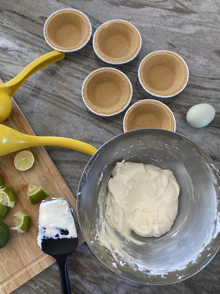 A picture of a mixing bowl with creamed goat and cream cheese mixed and a spatula sitting on a cutting board with the mixture