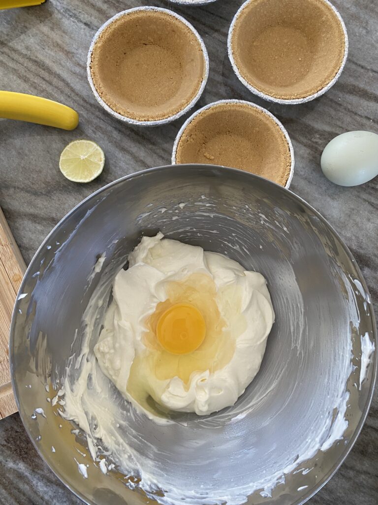 A picture of a mixing blow filled with mixed goat and cream cheese with an egg cracked over the top